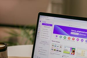 egy laptop monitor, melyen a közkedvelt canva weboldal részlete látszódik. A háttérben elmosottan egy szoba, iroda látszódik