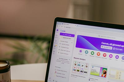 egy laptop monitor, melyen a közkedvelt canva weboldal részlete látszódik. A háttérben elmosottan egy szoba, iroda látszódik